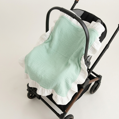 A mint green and white ruffled muslin baby blanket draped over a black stroller, photographed on a clean off-white studio background.