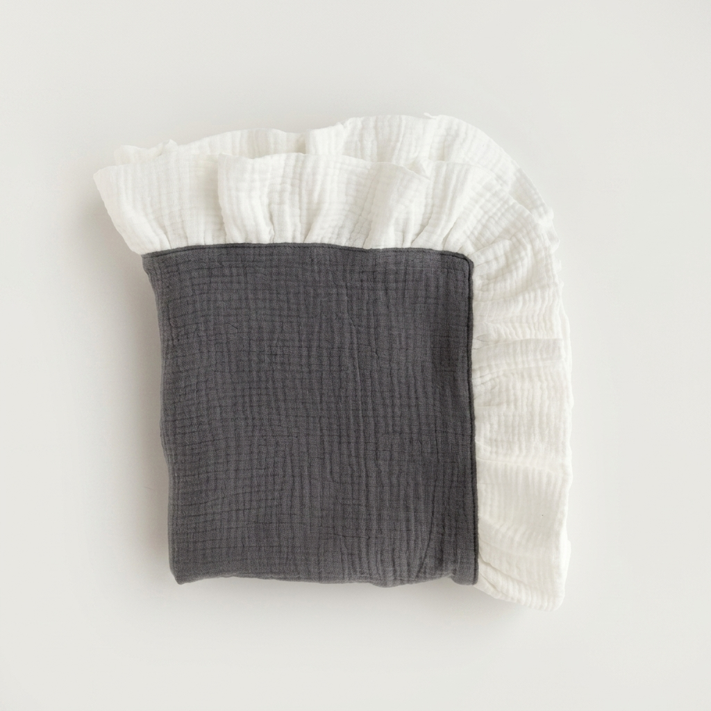 A folded muslin baby blanket or swaddle in dark gray and white, featuring a ruffled edge, photographed on a clean off-white background.