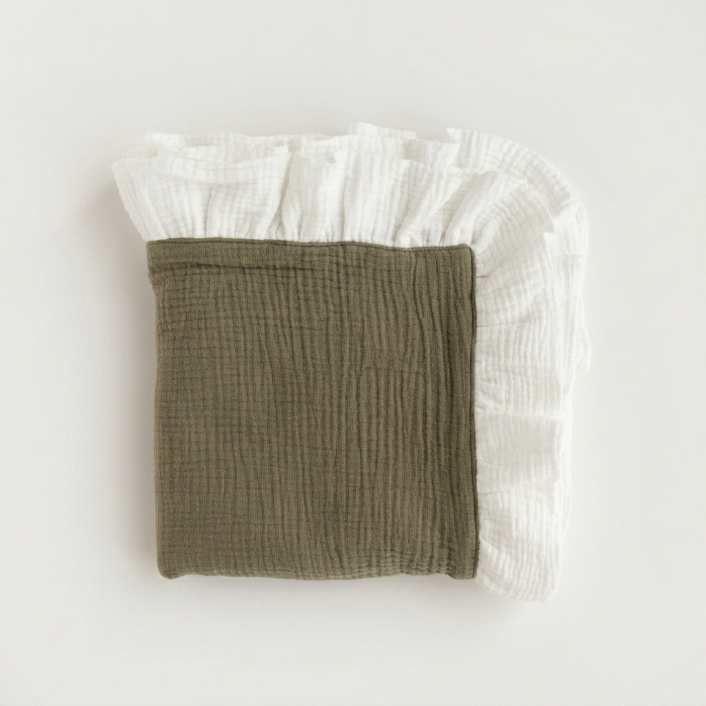 A folded muslin baby blanket in olive green with a white ruffled border, photographed flat on a light off-white background.