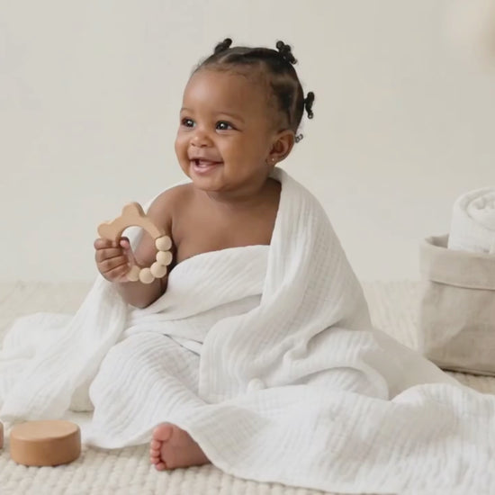 Baby DukWear organic white muslin swaddle blanket wrapped around a smiling baby in a cozy nursery