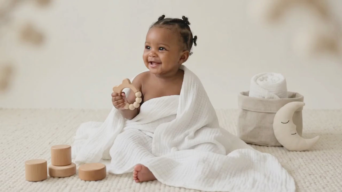 Baby DukWear organic white muslin swaddle blanket wrapped around a smiling baby in a cozy nursery